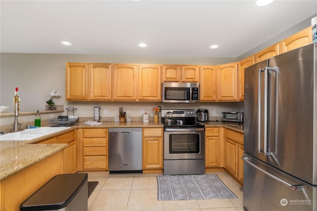 kitchen with stainless steel appliances, light stone counters, light brown cabinets, sink, and light tile patterned flooring