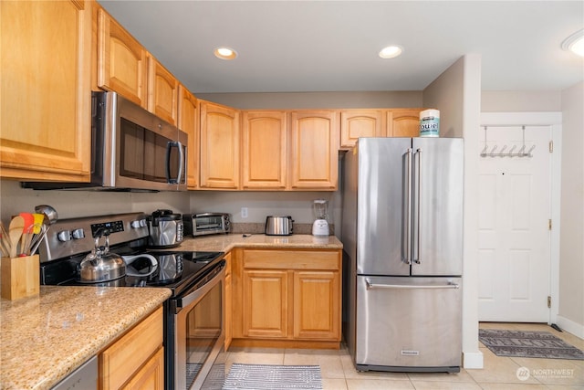 kitchen featuring stainless steel appliances, light brown cabinetry, light stone countertops, and light tile patterned floors