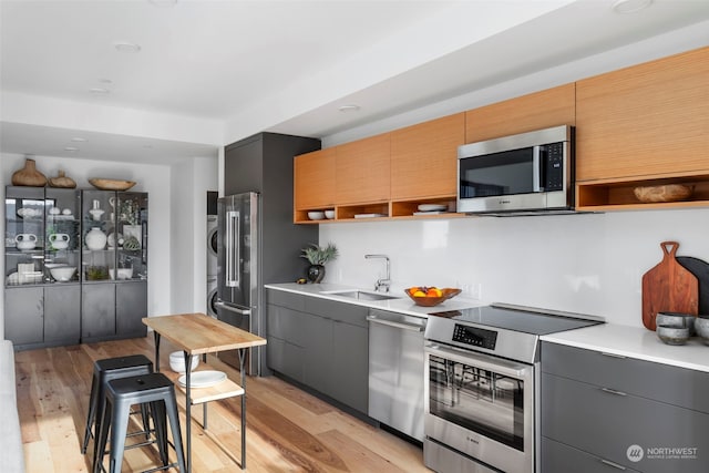 kitchen featuring light hardwood / wood-style floors, stainless steel appliances, a kitchen bar, sink, and stacked washer and dryer