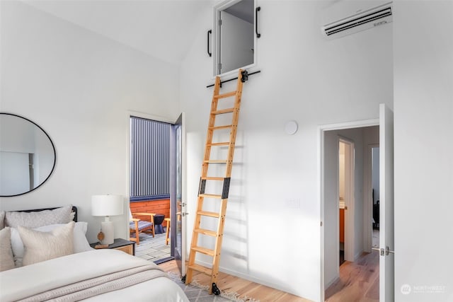 bedroom featuring high vaulted ceiling, an AC wall unit, and light hardwood / wood-style flooring