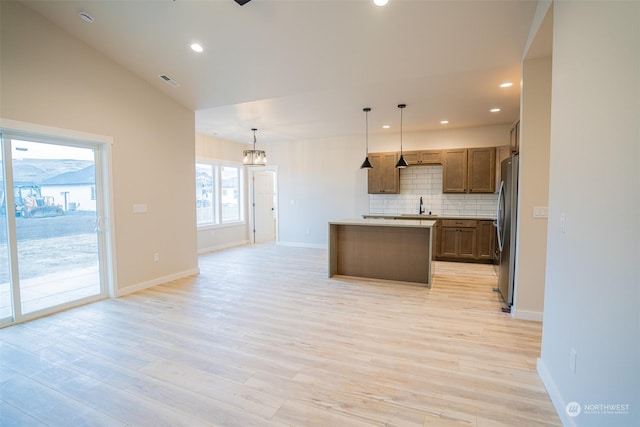 kitchen featuring hanging light fixtures, stainless steel fridge, a kitchen island, light hardwood / wood-style flooring, and lofted ceiling