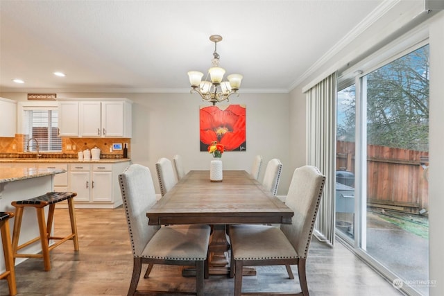 dining area with crown molding, a notable chandelier, and light wood-type flooring