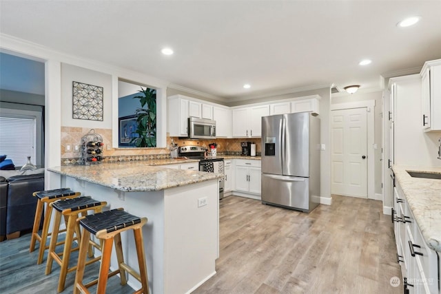 kitchen with white cabinetry, light stone counters, a breakfast bar area, and stainless steel appliances