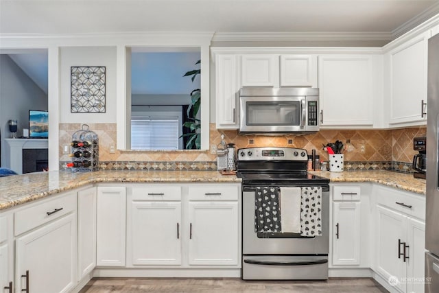 kitchen with stainless steel appliances, tasteful backsplash, light stone countertops, ornamental molding, and white cabinets