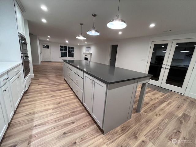 kitchen with hanging light fixtures, light wood-type flooring, a center island, stainless steel double oven, and white cabinets