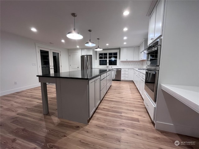 kitchen with appliances with stainless steel finishes, a kitchen island, white cabinetry, decorative light fixtures, and tasteful backsplash