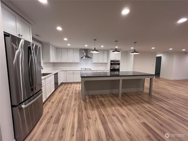 kitchen with light hardwood / wood-style flooring, pendant lighting, stainless steel appliances, wall chimney range hood, and white cabinetry