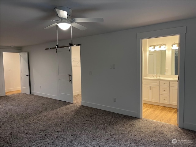 unfurnished bedroom with sink, connected bathroom, ceiling fan, a barn door, and light colored carpet