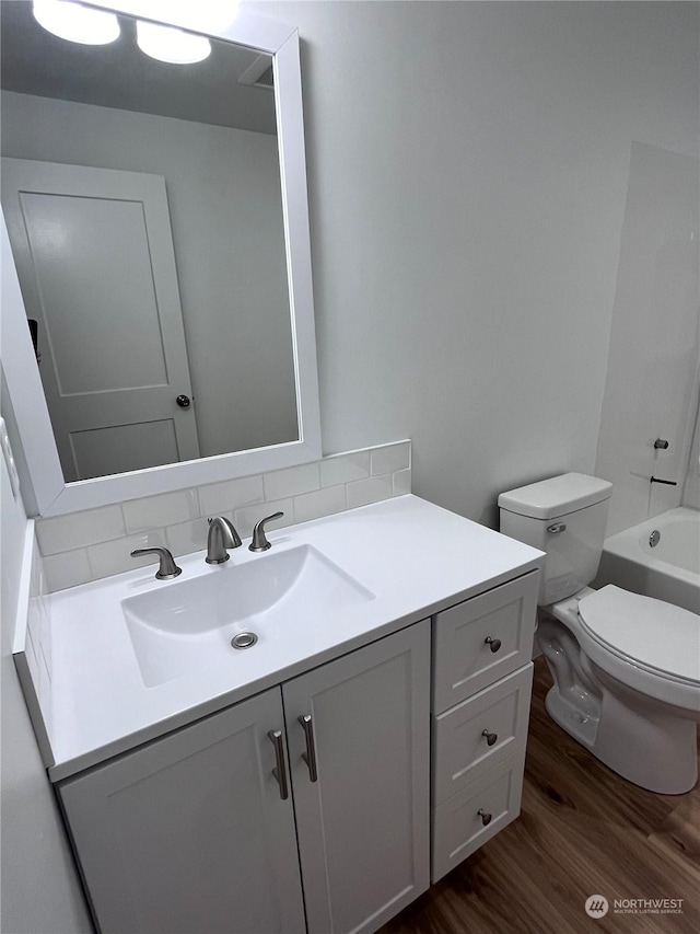 bathroom featuring toilet, wood-type flooring, vanity, and backsplash