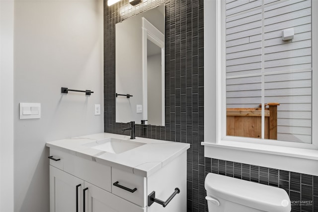 bathroom with toilet, vanity, and tile walls