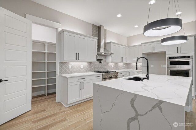 kitchen with sink, white cabinetry, light stone counters, and wall chimney exhaust hood