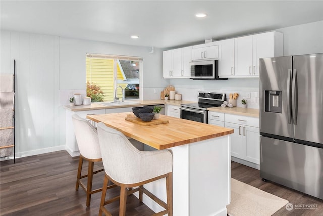 kitchen featuring appliances with stainless steel finishes, butcher block counters, a kitchen breakfast bar, a center island, and white cabinets