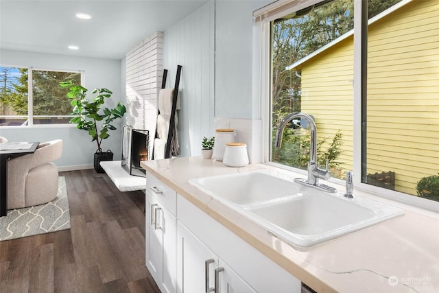 kitchen with a large fireplace, sink, white cabinets, and dark hardwood / wood-style flooring