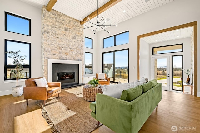 living room featuring wood finished floors, a high ceiling, a stone fireplace, wooden ceiling, and beamed ceiling