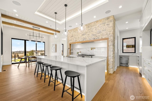 kitchen with a raised ceiling, white cabinets, beverage cooler, and light wood finished floors