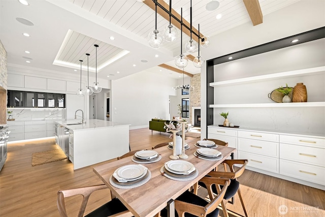 dining space featuring beam ceiling, wood ceiling, light wood finished floors, and a large fireplace