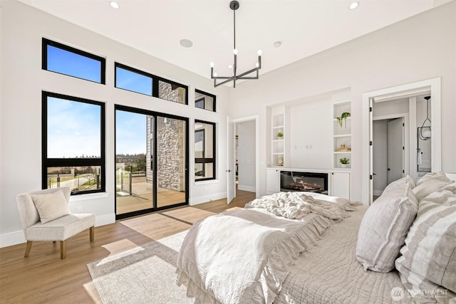 bedroom featuring baseboards, light wood-style floors, a glass covered fireplace, access to outside, and a chandelier