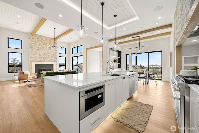 kitchen with a sink, a stone fireplace, appliances with stainless steel finishes, light wood finished floors, and a large island with sink