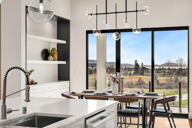 kitchen featuring a sink, open shelves, light stone counters, white cabinetry, and hanging light fixtures