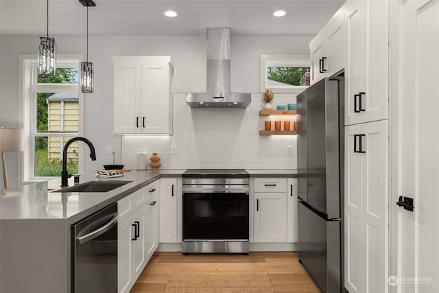 kitchen with decorative light fixtures, stainless steel appliances, wall chimney range hood, white cabinets, and sink