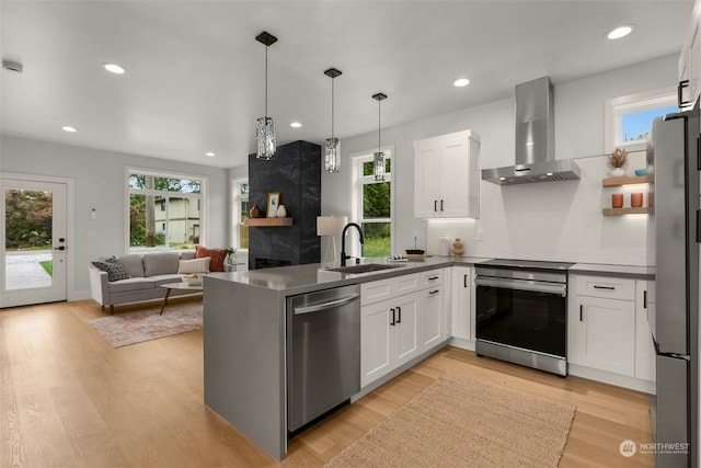 kitchen featuring appliances with stainless steel finishes, hanging light fixtures, white cabinets, wall chimney range hood, and sink