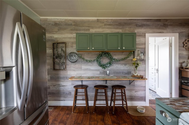 kitchen featuring dark hardwood / wood-style floors, stainless steel fridge, green cabinetry, wooden walls, and a kitchen bar