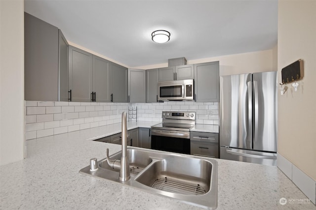 kitchen featuring sink, appliances with stainless steel finishes, gray cabinets, light stone countertops, and backsplash