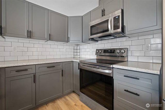 kitchen with light hardwood / wood-style flooring, gray cabinets, stainless steel appliances, light stone countertops, and decorative backsplash