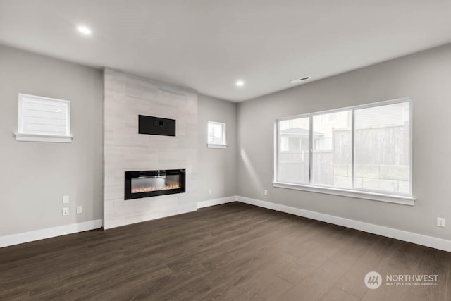 unfurnished living room featuring a tiled fireplace and dark hardwood / wood-style floors