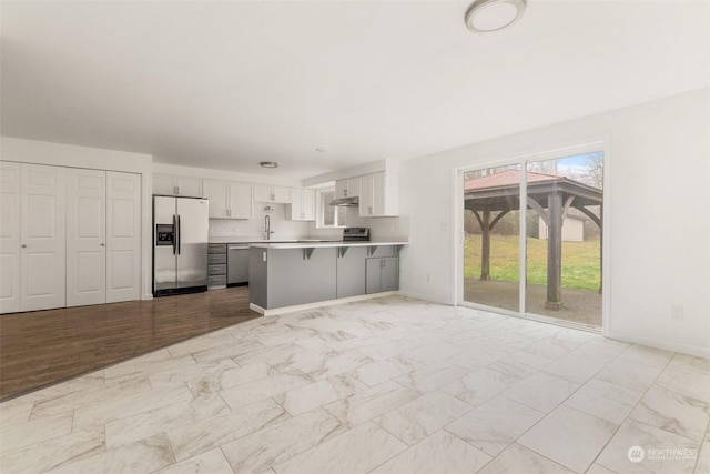 kitchen with kitchen peninsula, decorative backsplash, a kitchen bar, white cabinetry, and appliances with stainless steel finishes