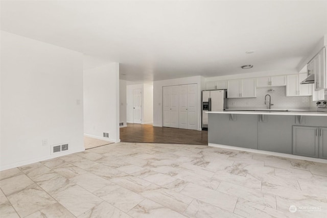 kitchen with stainless steel refrigerator with ice dispenser, white cabinetry, tasteful backsplash, kitchen peninsula, and a breakfast bar area