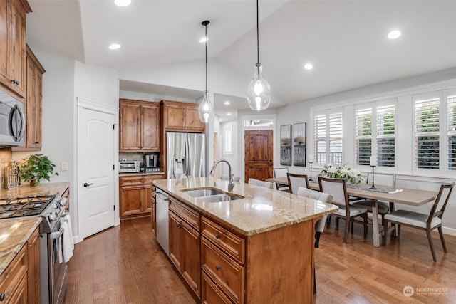 kitchen with appliances with stainless steel finishes, an island with sink, sink, backsplash, and hanging light fixtures