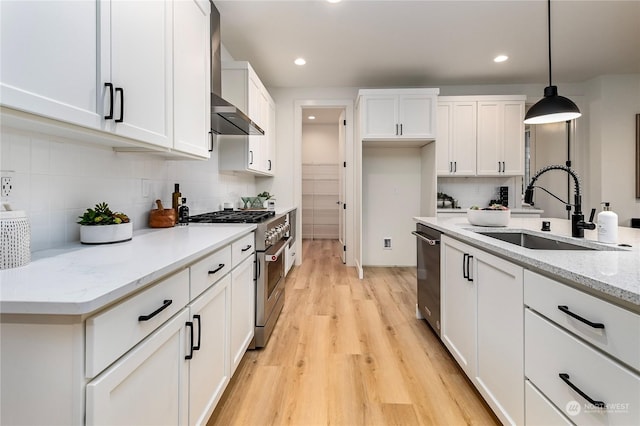 kitchen with white cabinets, stainless steel appliances, light stone counters, sink, and decorative light fixtures