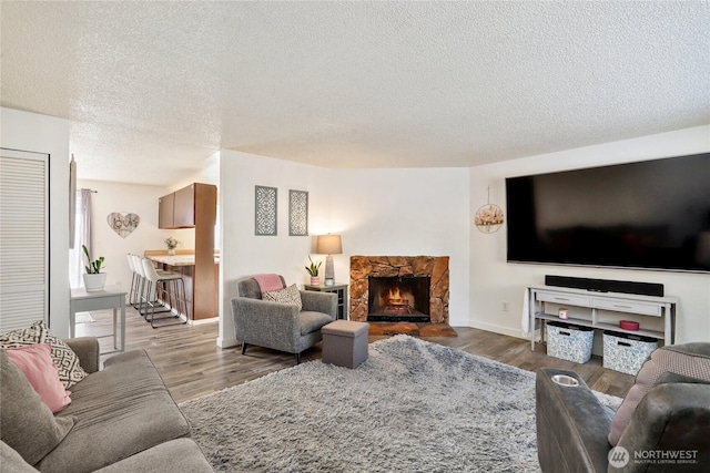 living room with a stone fireplace, light hardwood / wood-style flooring, and a textured ceiling