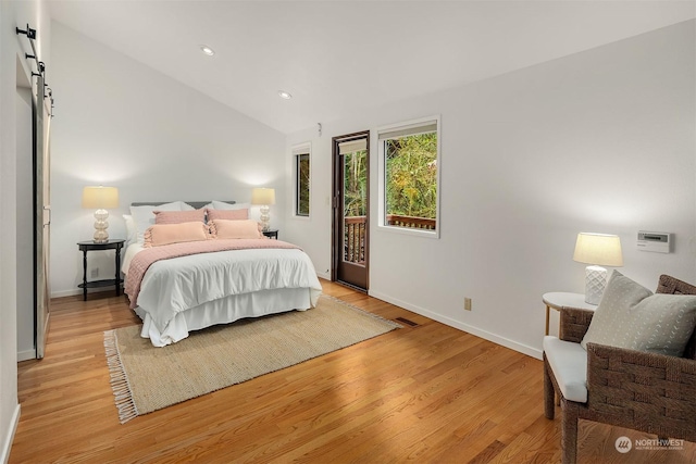 bedroom with vaulted ceiling, a barn door, and light wood-type flooring