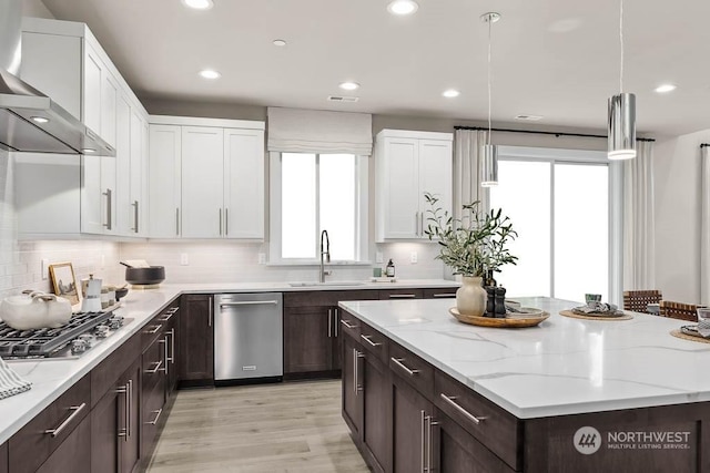 kitchen with white cabinets, wall chimney range hood, pendant lighting, and sink