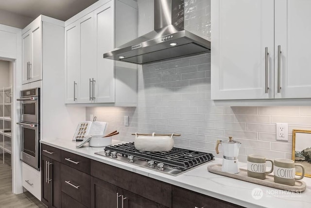 kitchen with white cabinetry, decorative backsplash, dark brown cabinetry, wall chimney range hood, and appliances with stainless steel finishes