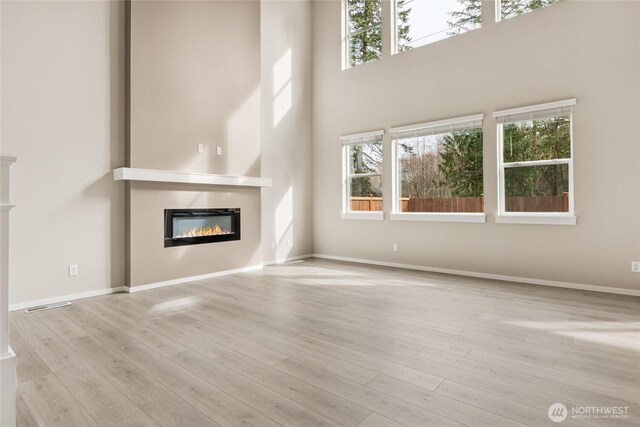 unfurnished living room featuring a glass covered fireplace, plenty of natural light, wood finished floors, and visible vents