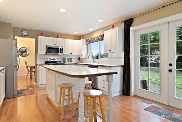 kitchen with a kitchen island, a breakfast bar, white cabinets, backsplash, and stainless steel appliances