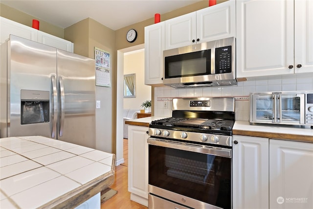 kitchen featuring white cabinetry, tile counters, stainless steel appliances, light hardwood / wood-style floors, and backsplash