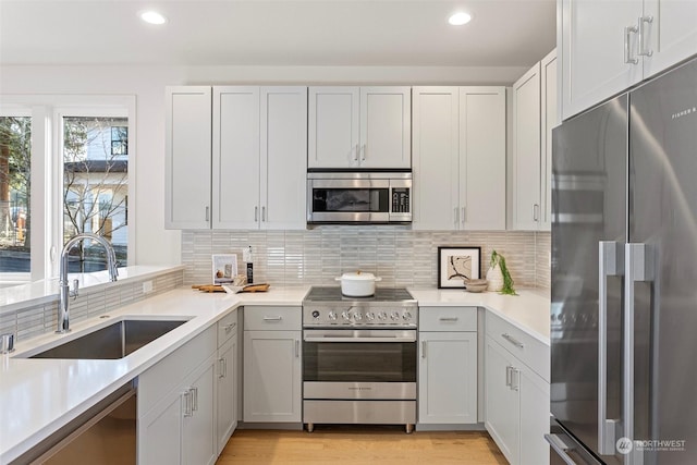 kitchen featuring sink, light wood-type flooring, high end appliances, and tasteful backsplash