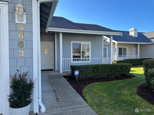 view of exterior entry featuring a lawn and covered porch