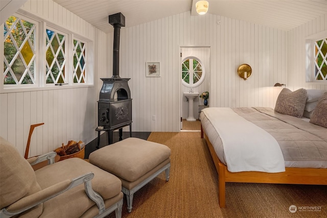 carpeted bedroom featuring a wood stove, vaulted ceiling, and multiple windows