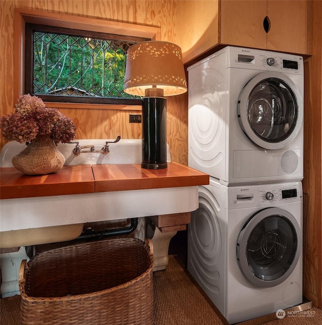 laundry area featuring cabinets, stacked washer / dryer, and wood walls