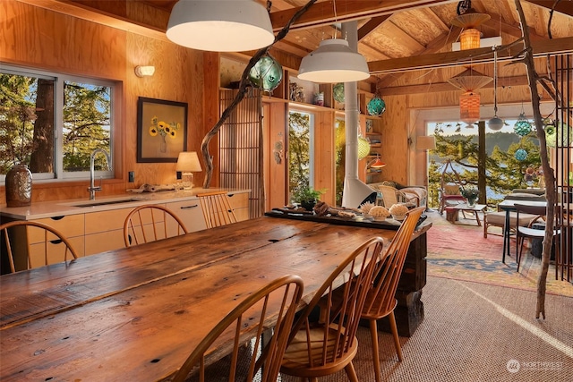 dining space with sink, lofted ceiling with beams, light colored carpet, wood ceiling, and wood walls