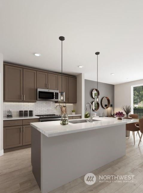 kitchen featuring appliances with stainless steel finishes, hanging light fixtures, an island with sink, and sink