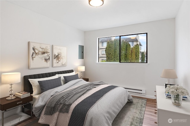 bedroom featuring electric panel, hardwood / wood-style floors, and a baseboard heating unit