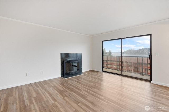 unfurnished living room with baseboards, a tile fireplace, light wood-style floors, and crown molding