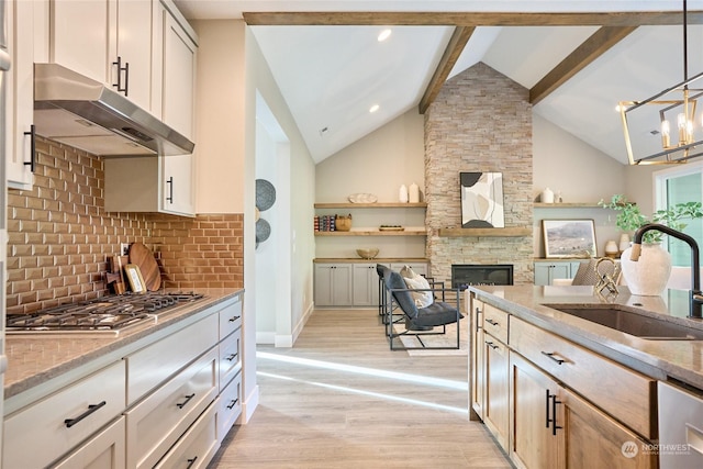 kitchen featuring pendant lighting, sink, decorative backsplash, vaulted ceiling with beams, and a stone fireplace