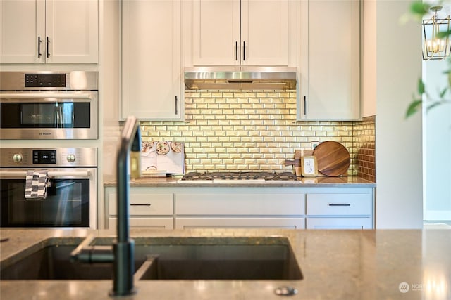 kitchen with light stone countertops, white cabinetry, stainless steel double oven, and decorative backsplash